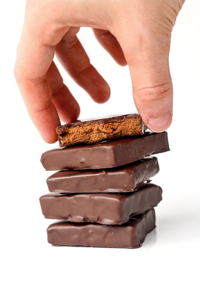 Holding a protein bar over a stack of four other bars.