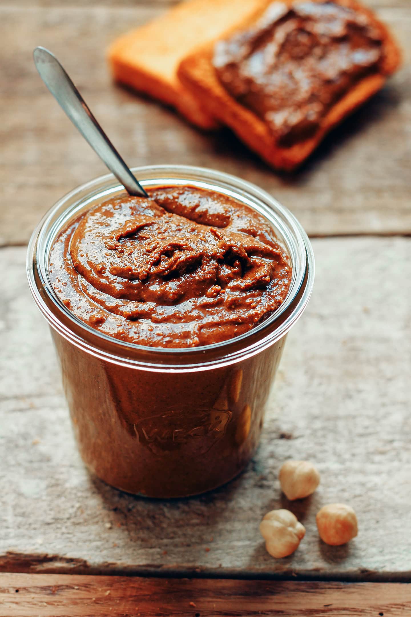 Glass jar containing chocolate praline spread on a rustic wood table.