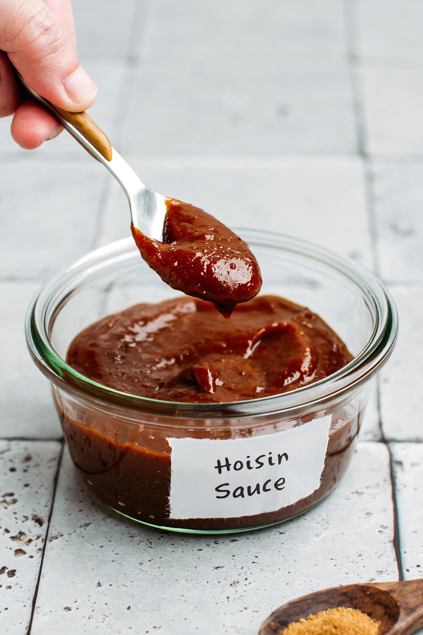 Holding a spoonful of hoisin sauce over a glass jar.