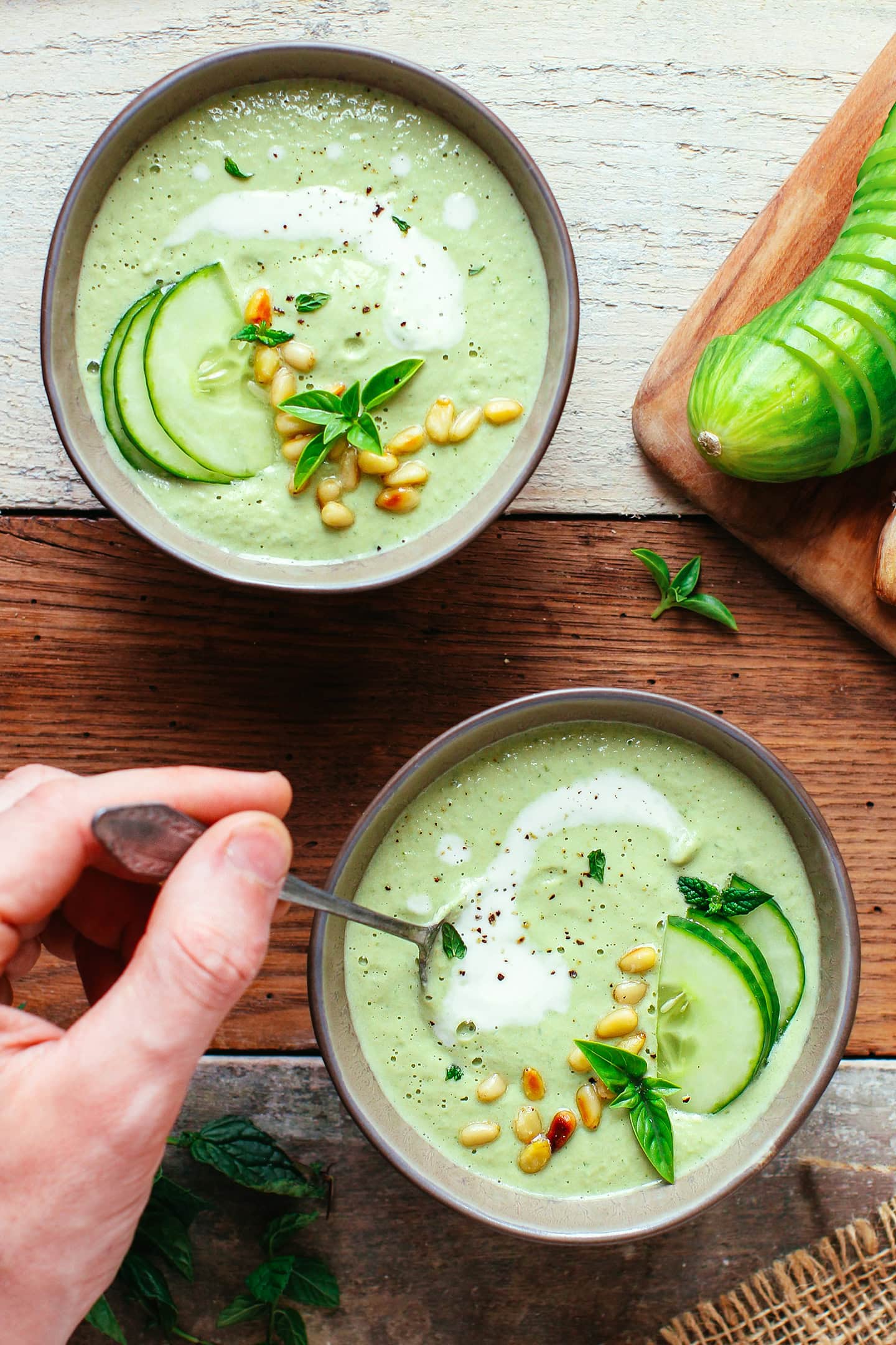 Two bowls of cucumber gazpacho topped with pine nuts and cucumber slices.