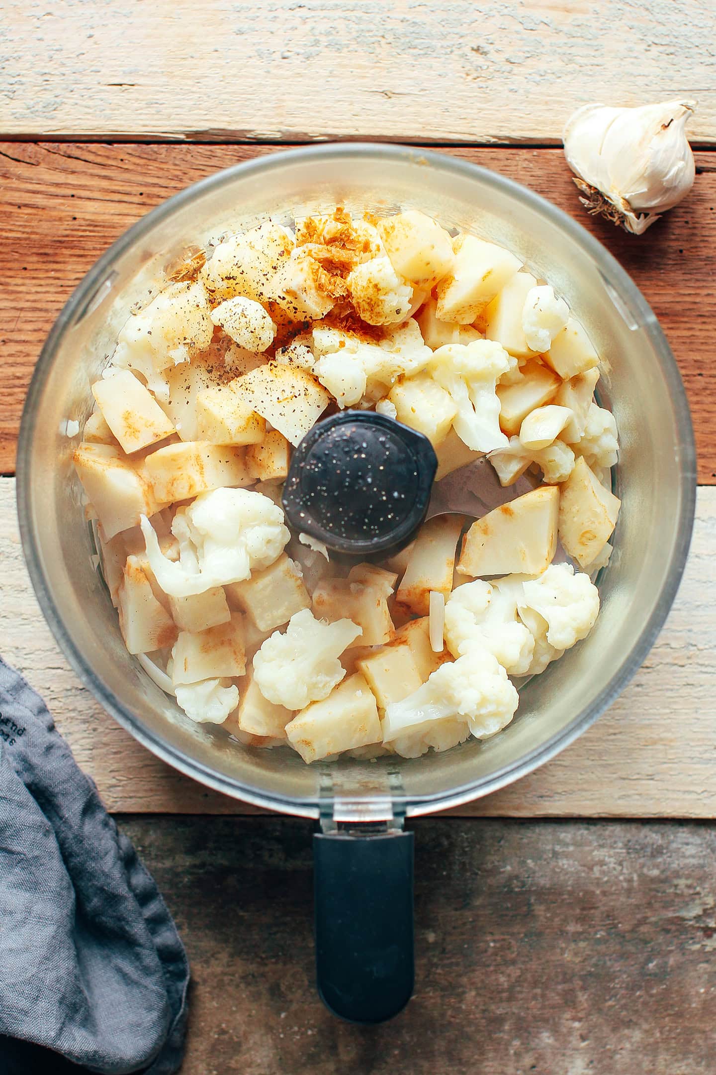 Cooked celery root and cauliflower in the bowl of a food processor.