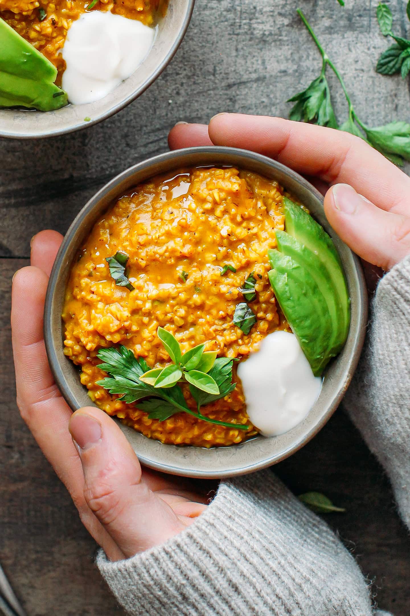 Holding a bowl of instant pot masala oats topped with avocado and herbs.