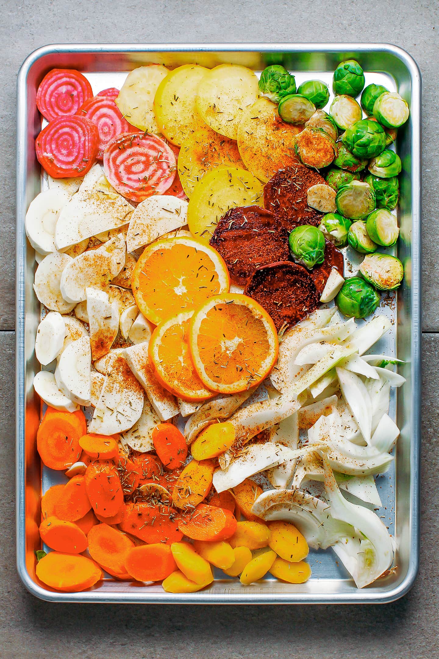 Raw vegetables coated with spices and oil on a baking sheet.
