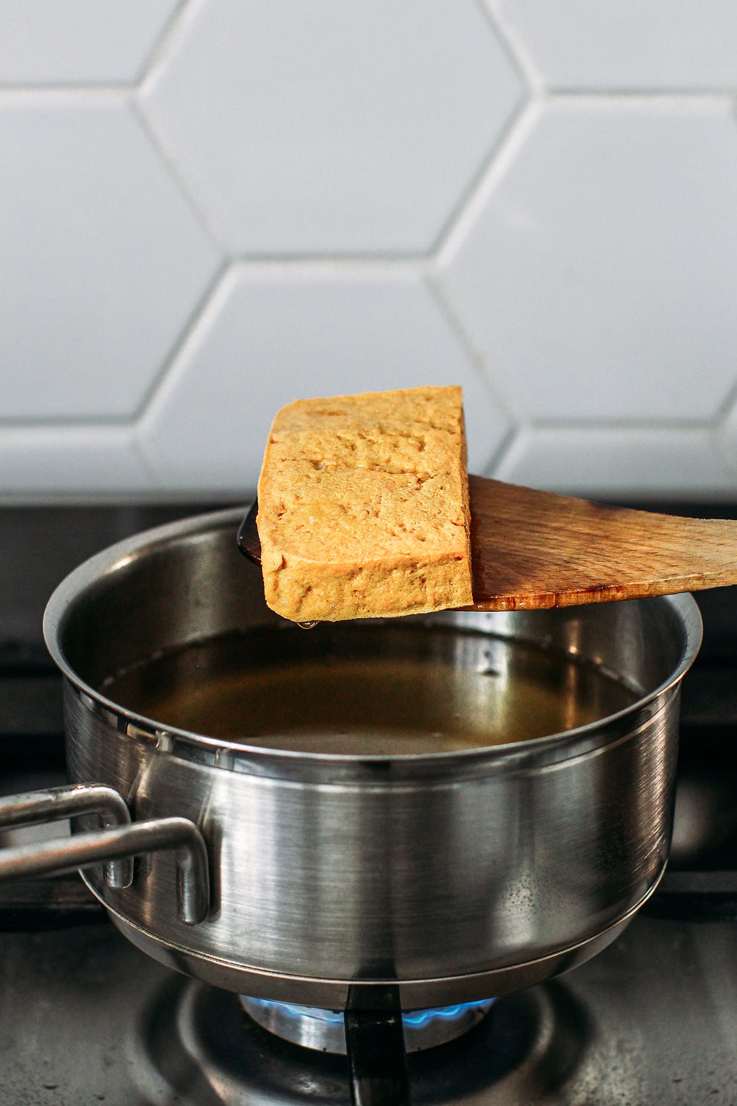 Holding a block of fried tofu over a pot of frying oil.