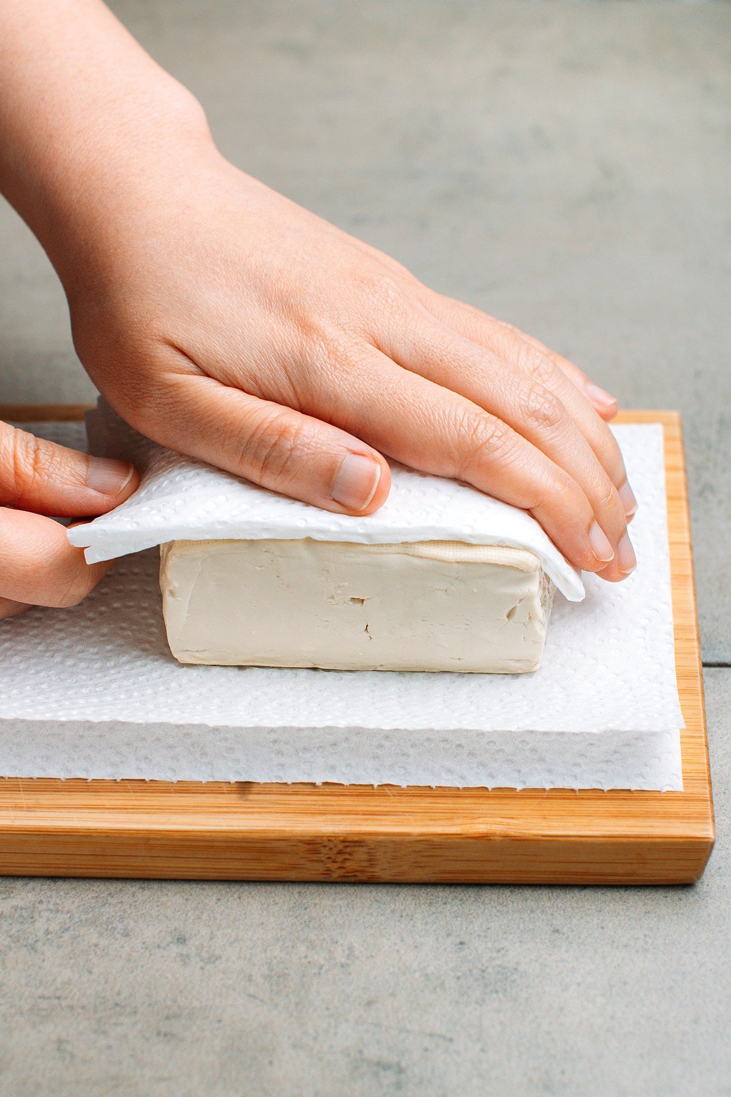 Pressing tofu between two sheets of kitchen paper towels.