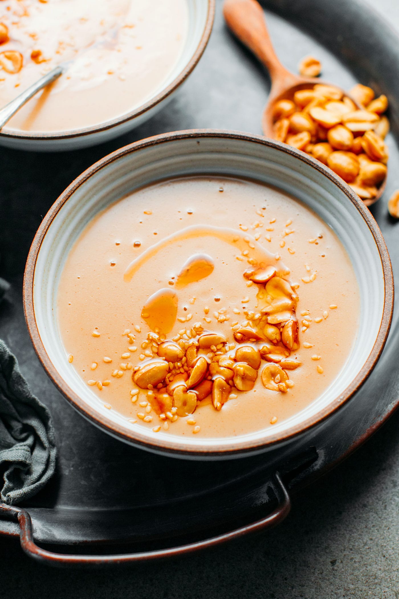 Bowl of peanut soup topped with roasted peanuts and toasted sesame seeds.