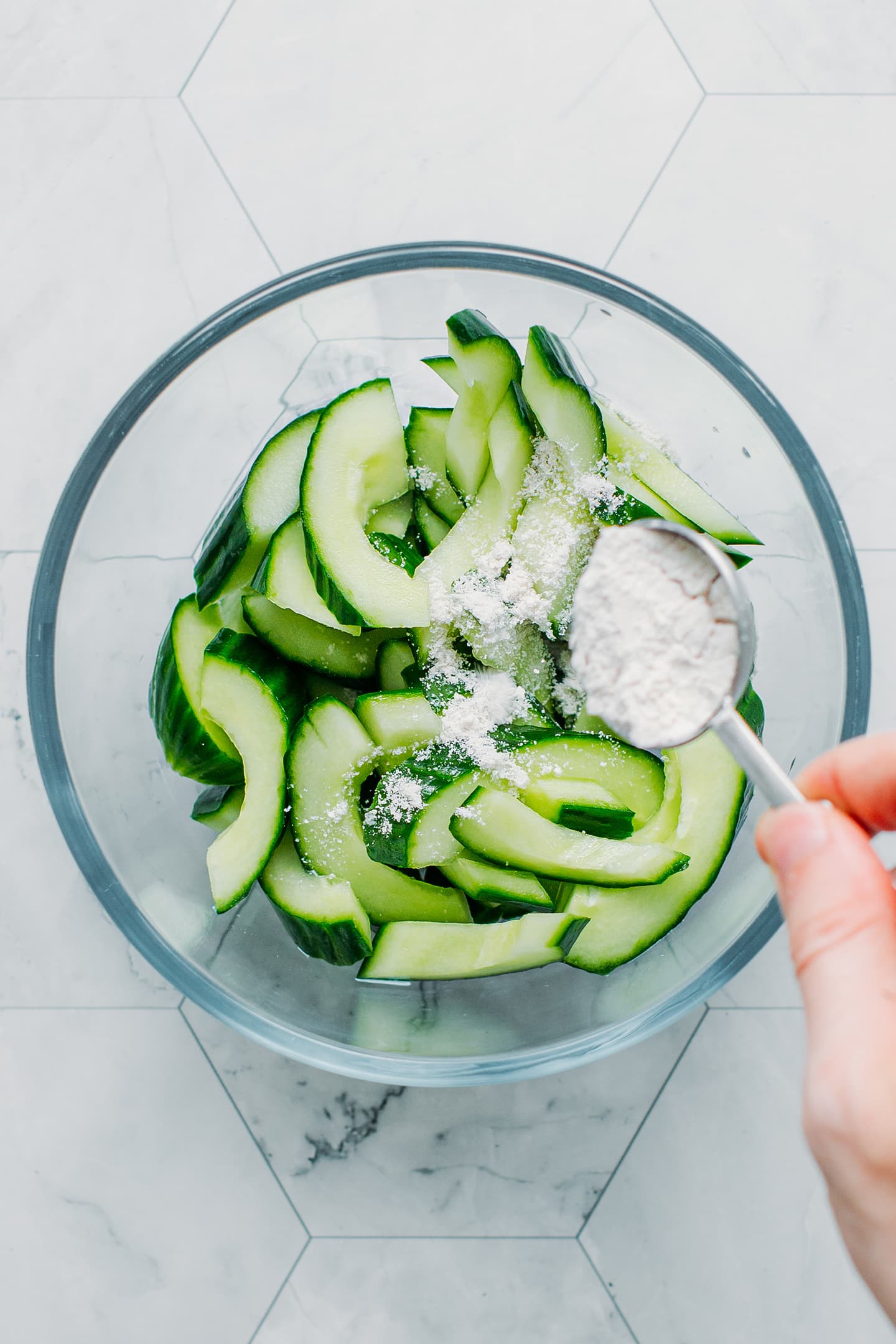 Sprinkling salt over sliced cucumbers.