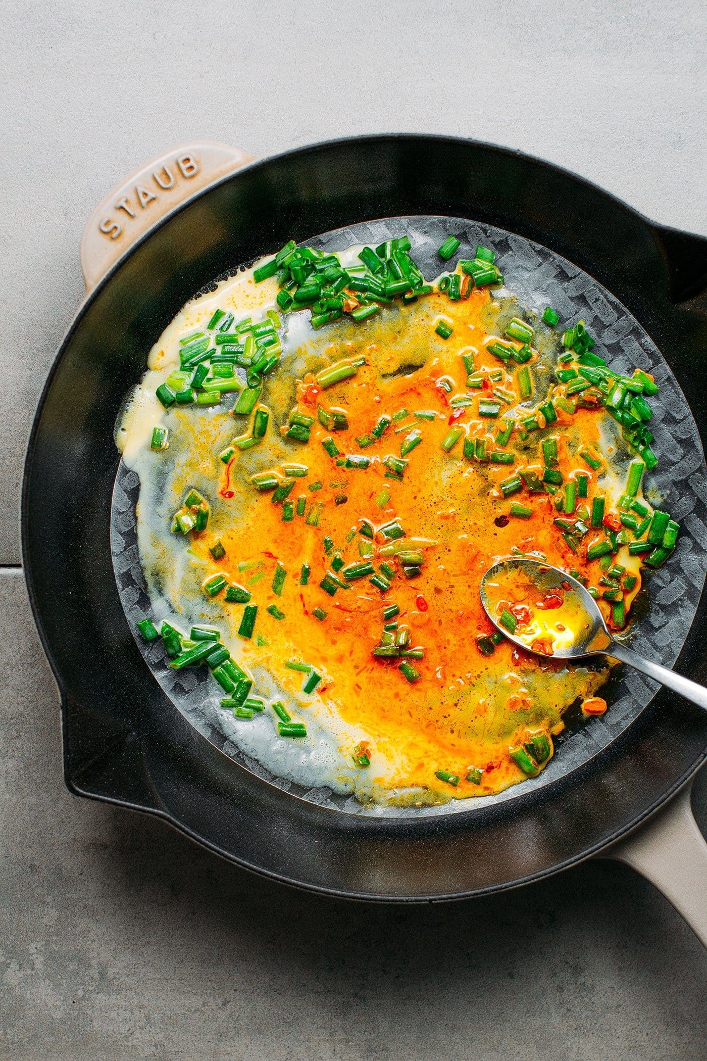 Green onions and vegan egg on a rice paper sheet in a skillet.