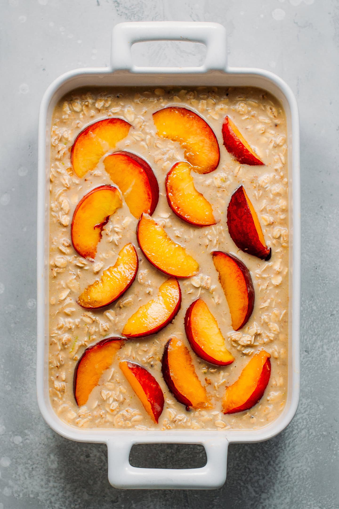 Oatmeal topped with sliced peaches in a baking pan.