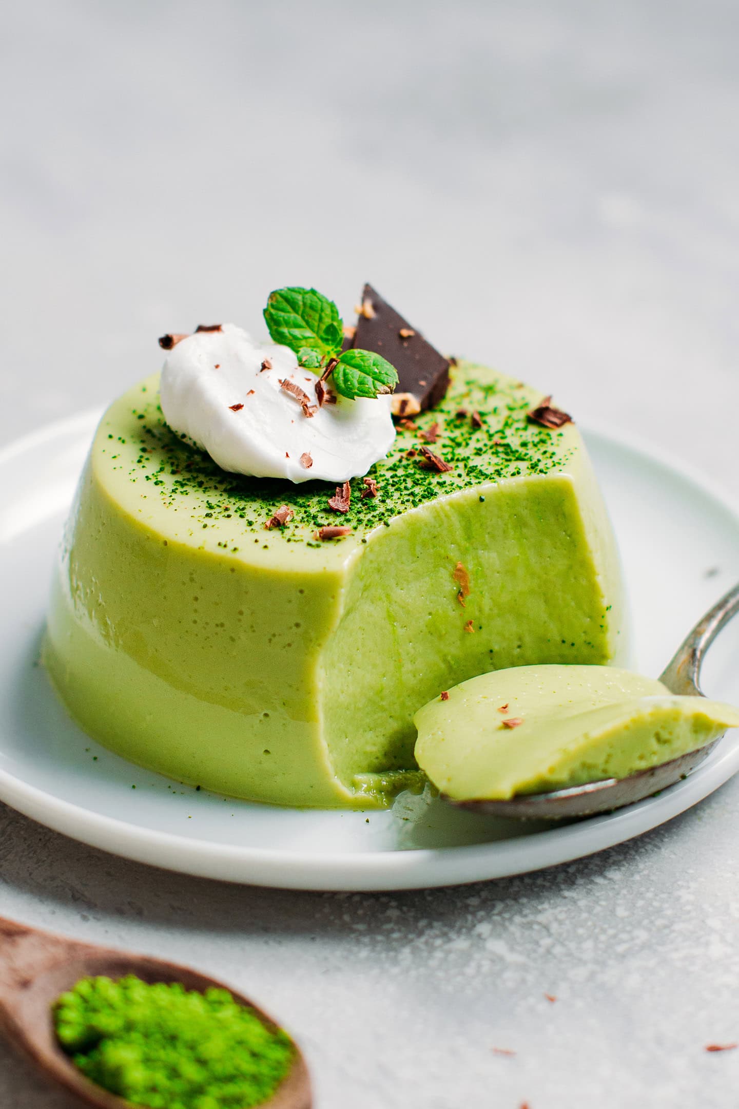 Matcha panna cotta topped with shaved dark chocolate, a dollop of coconut cream, and mint leaves.