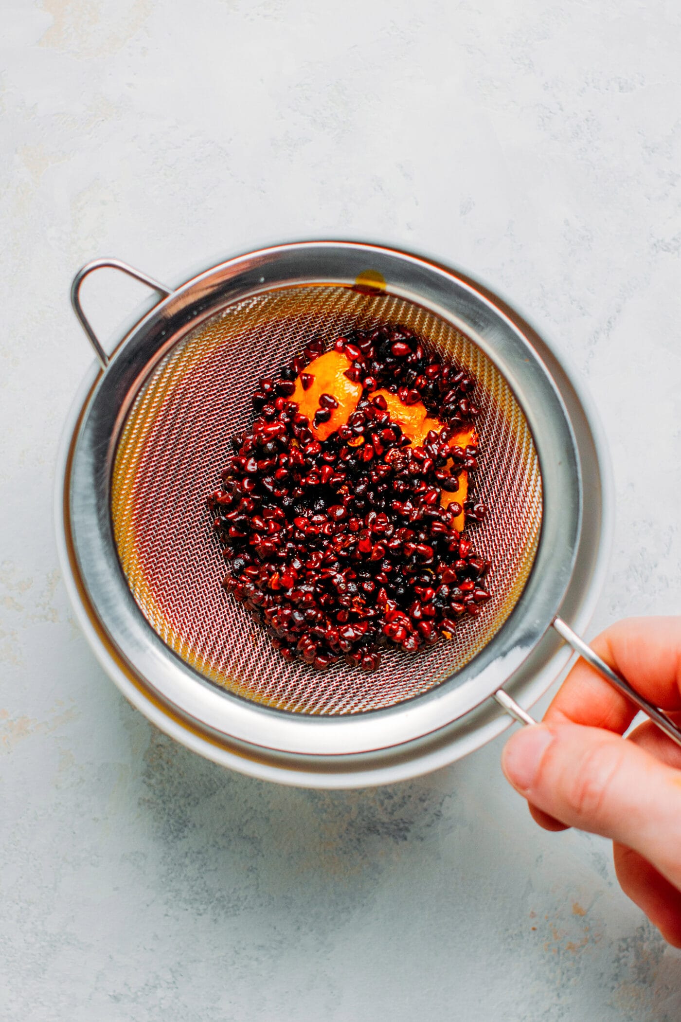 Straining annatto oil through a fine sieve mesh.