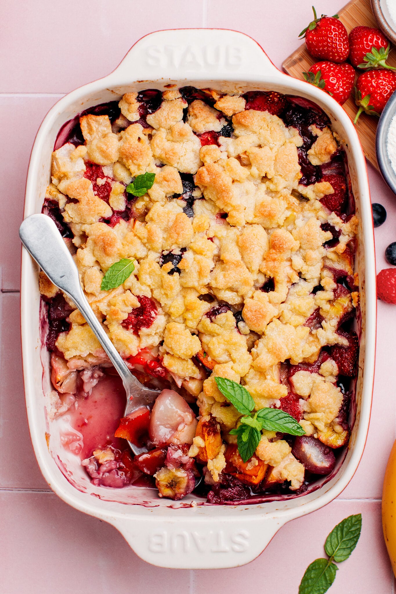 Fruit crumble in a baking dish with raspberries and mint leaves.