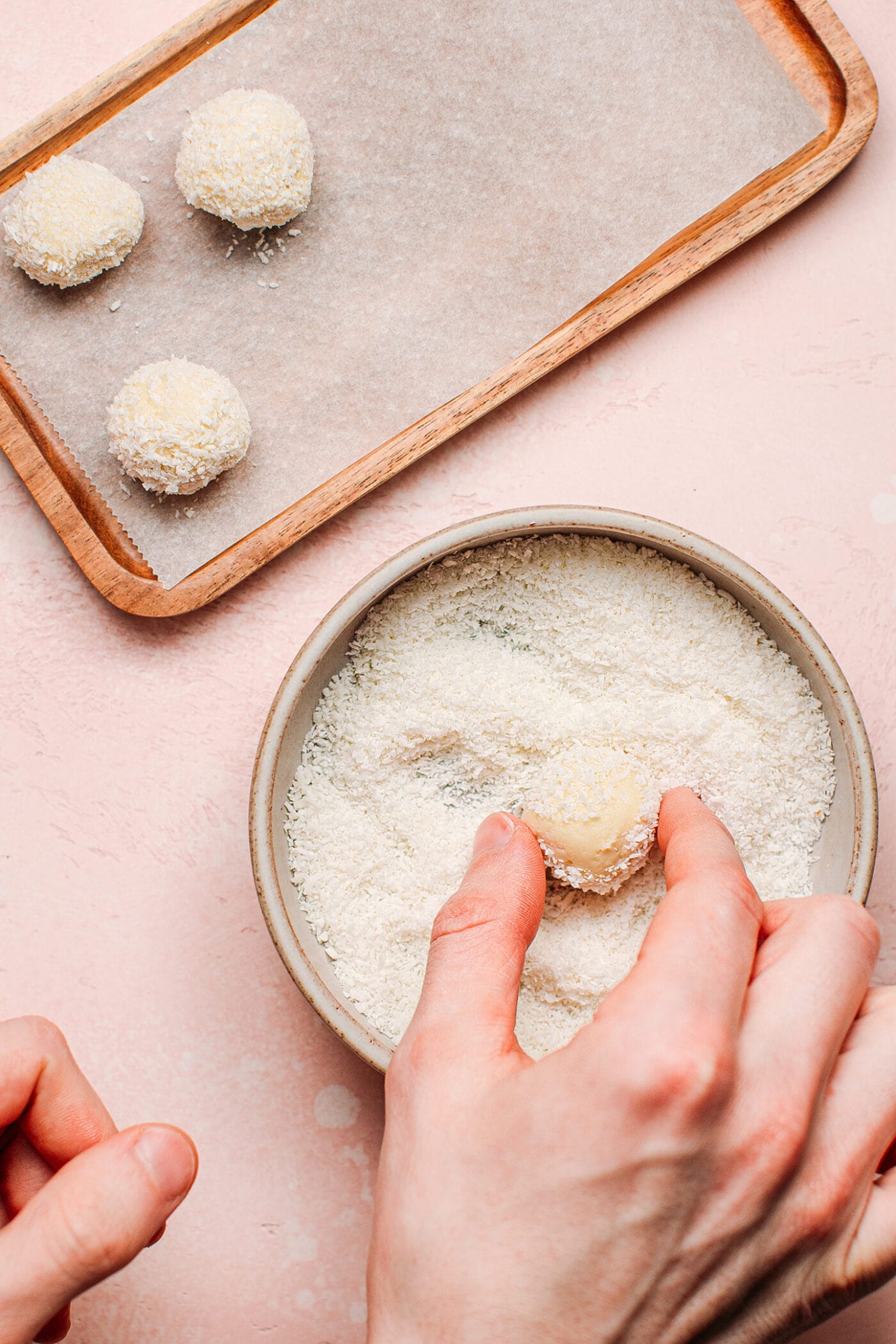 Coating vegan white chocolate truffles in shredded coconut.