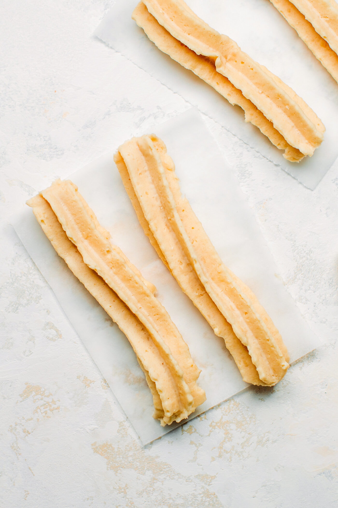 Vegan churros pipped on parchment paper.