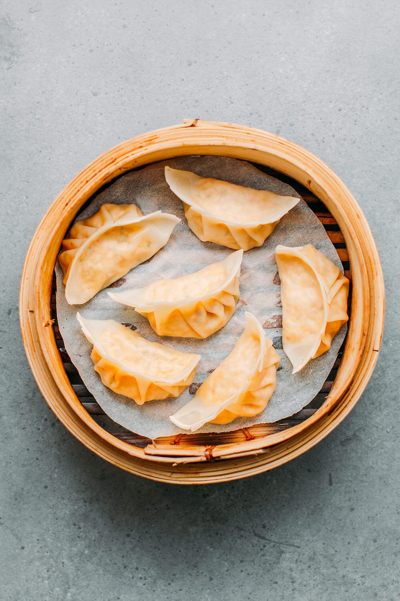 Cooked kimchi dumplings in a bamboo steamer basket.
