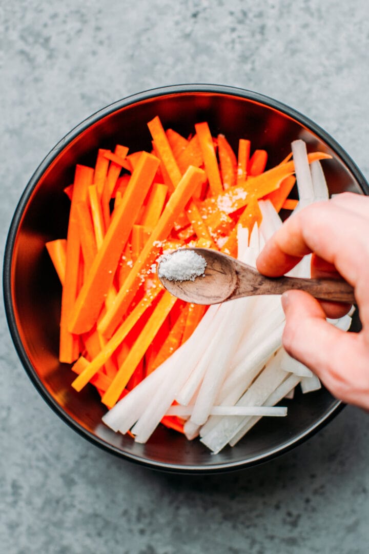 Sprinkling salt over carrots and daikon radish.