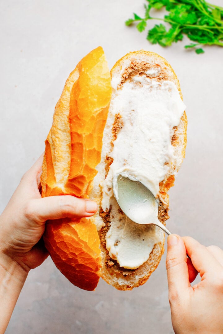 Spreading vegan mayo on a banh mi sandwich.