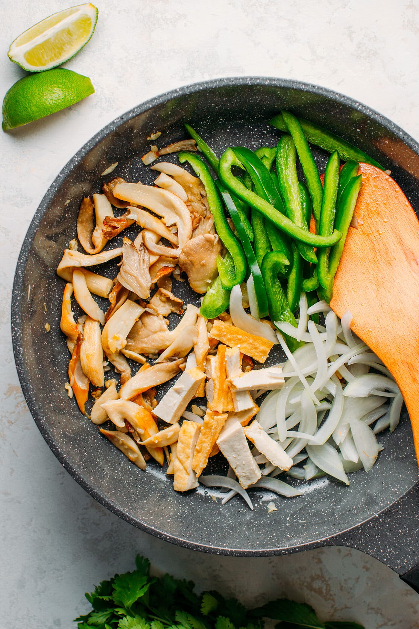 Sautéed mushrooms, green bell peppers, tofu, and onions in a skillet.