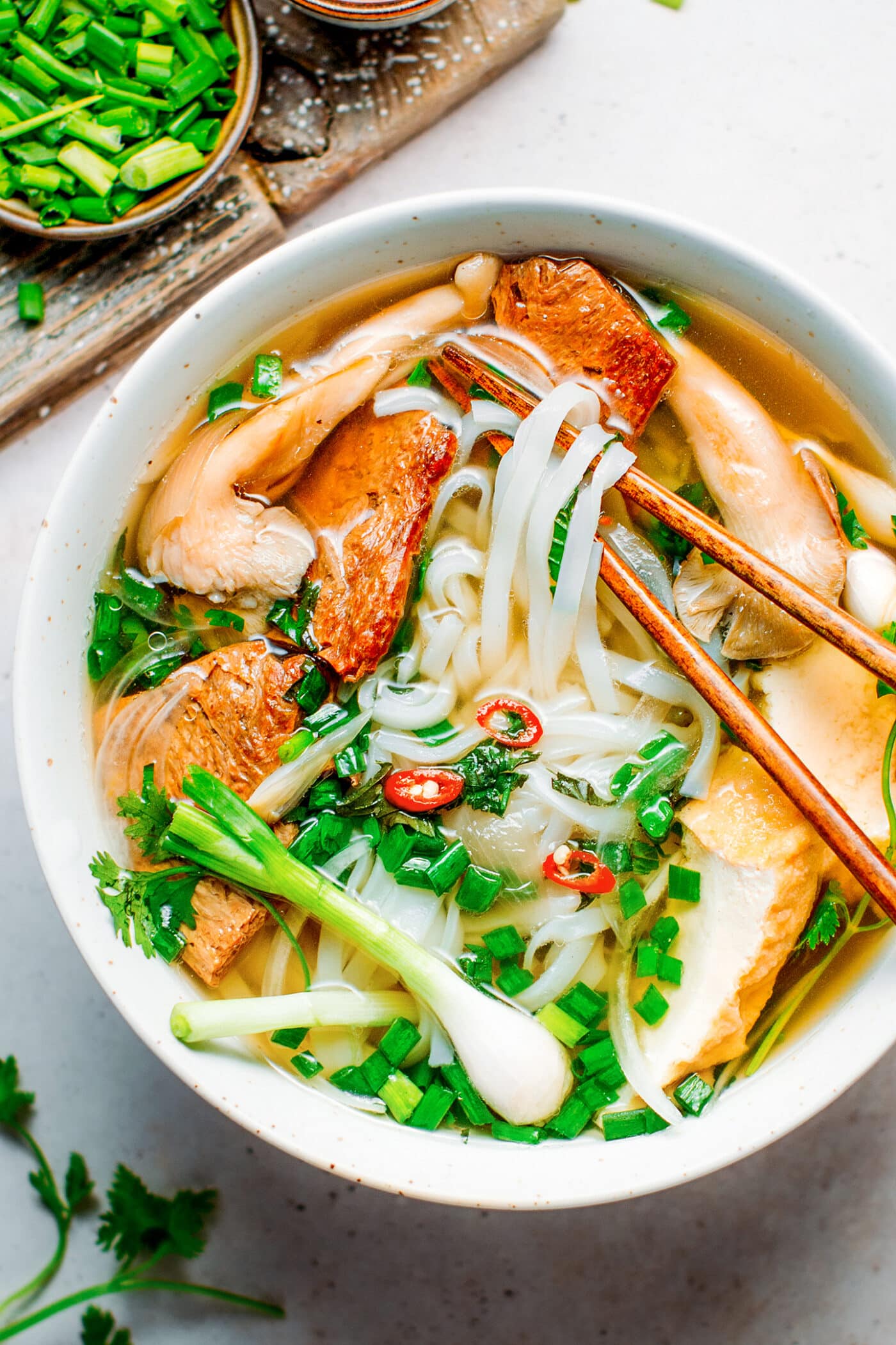 Bowl of vegan Pho with beef, tofu, mushrooms, and fresh herbs.