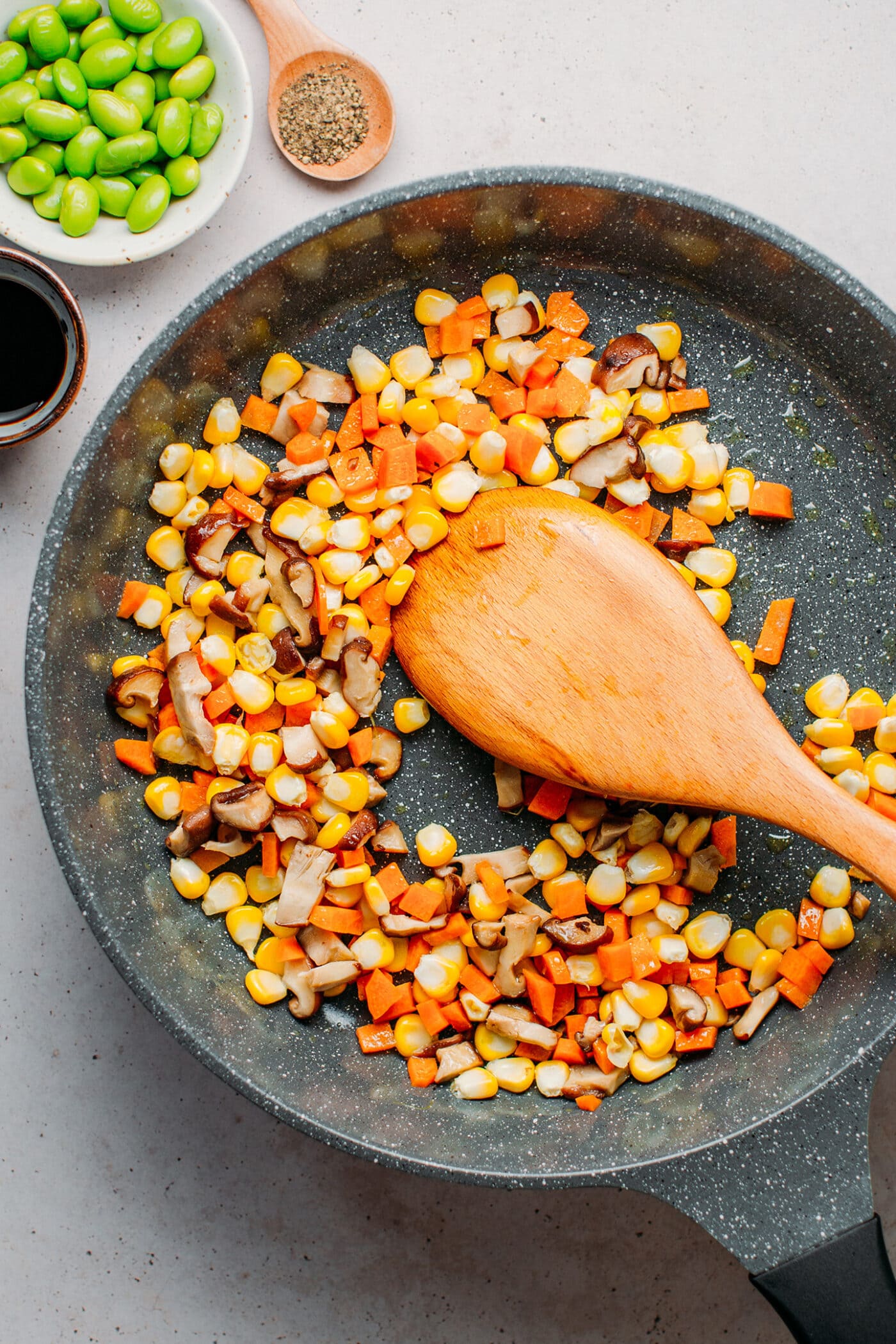 Cooking corn, carrots, and mushrooms in a skillet.