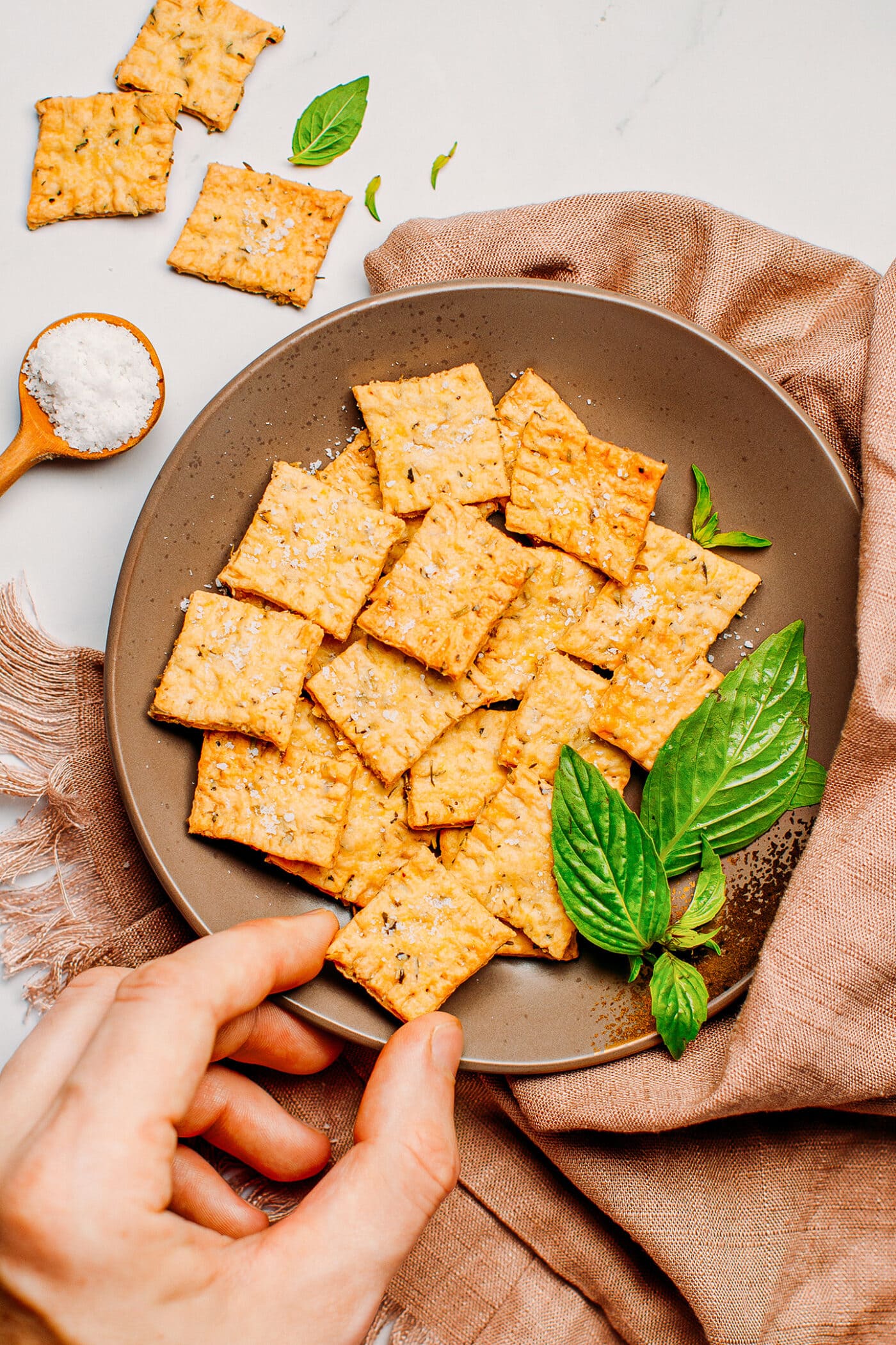Hand picking an herb cracker from a plate.