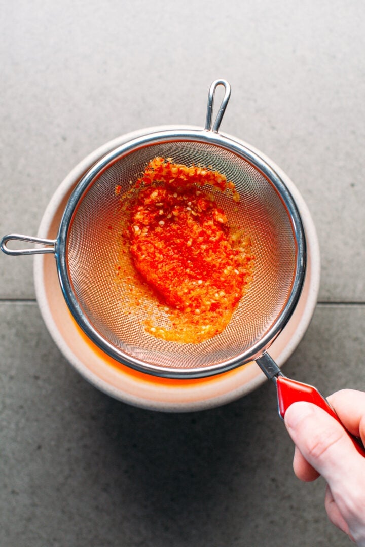 Straining chili pulp from chili sauce using a sieve.