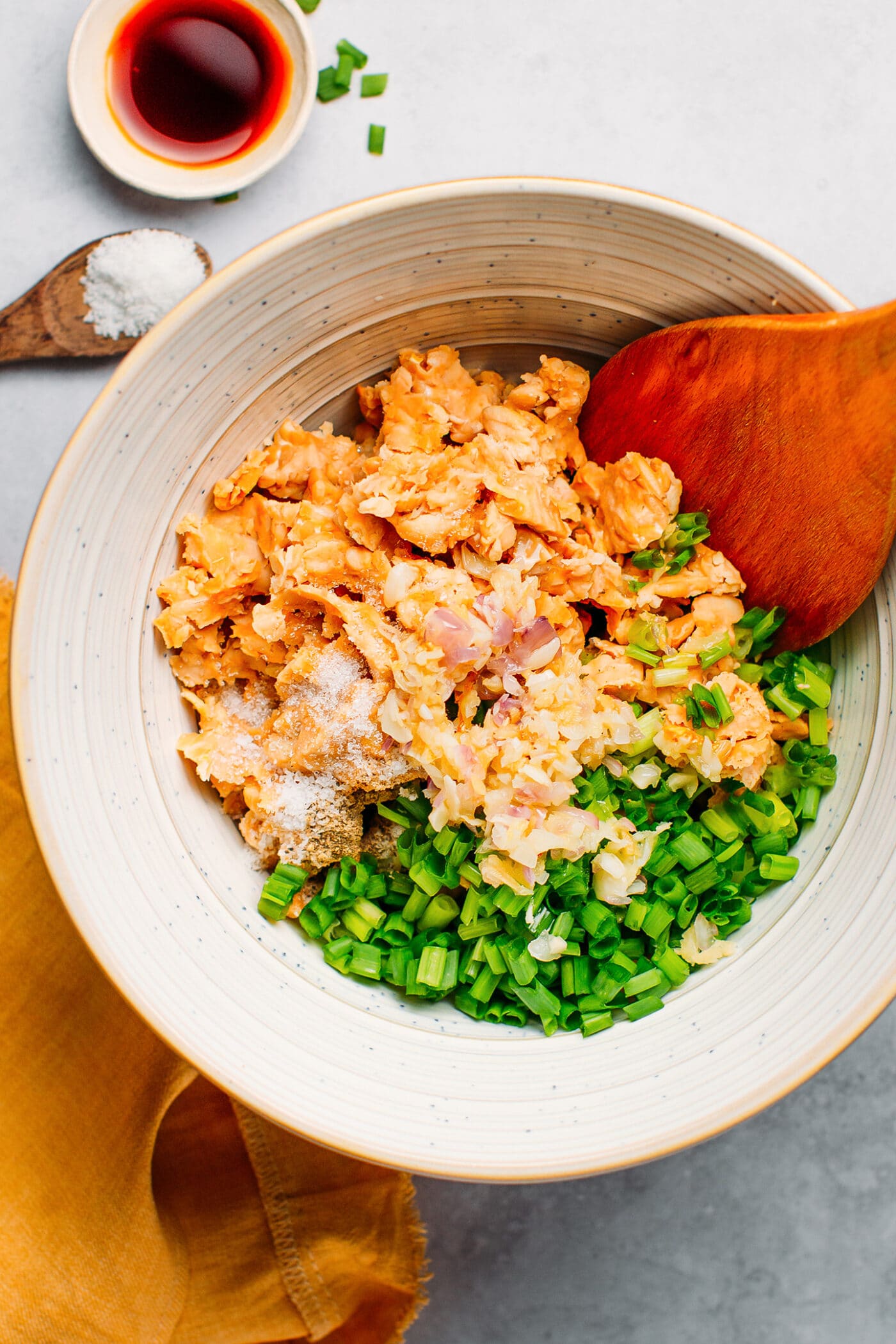 Mixing tempeh with garlic, ginger, shallots, and onions in a bowl.