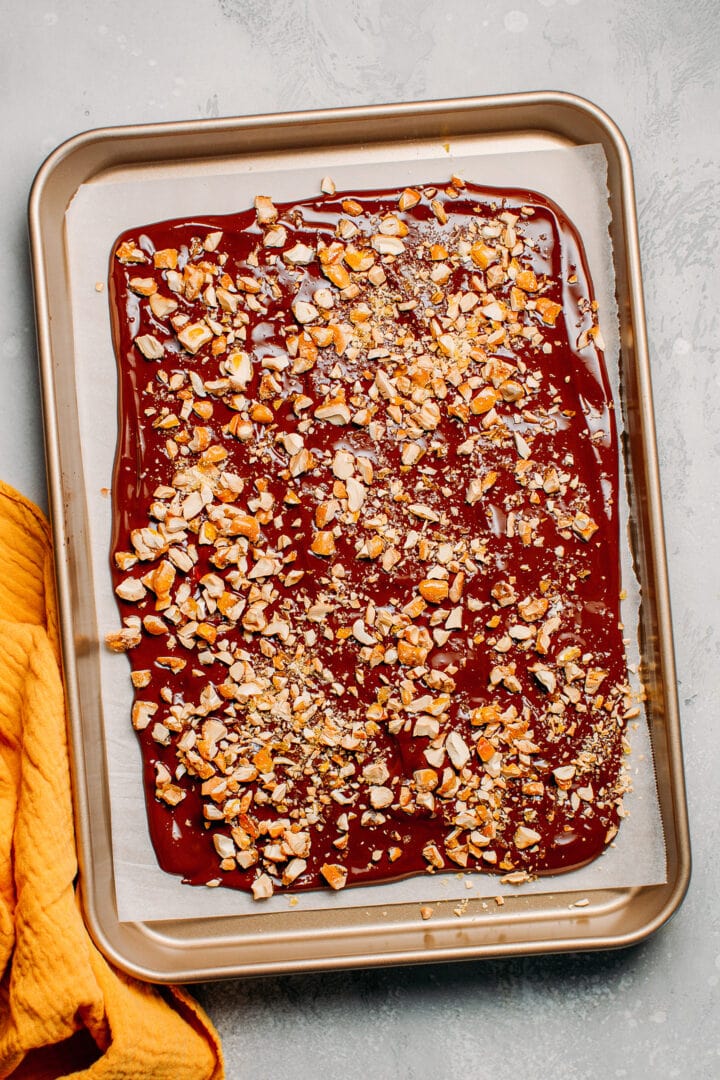 Melted chocolate spread on a baking sheet and topped with nuts.
