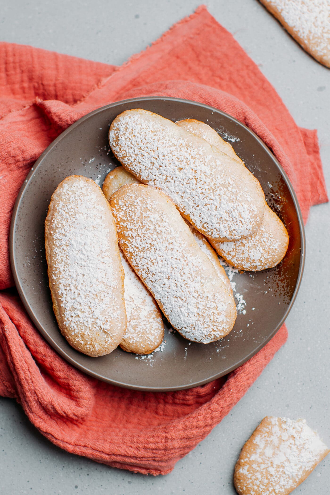 Vegan ladyfingers dusted with powdered sugar on a plate.