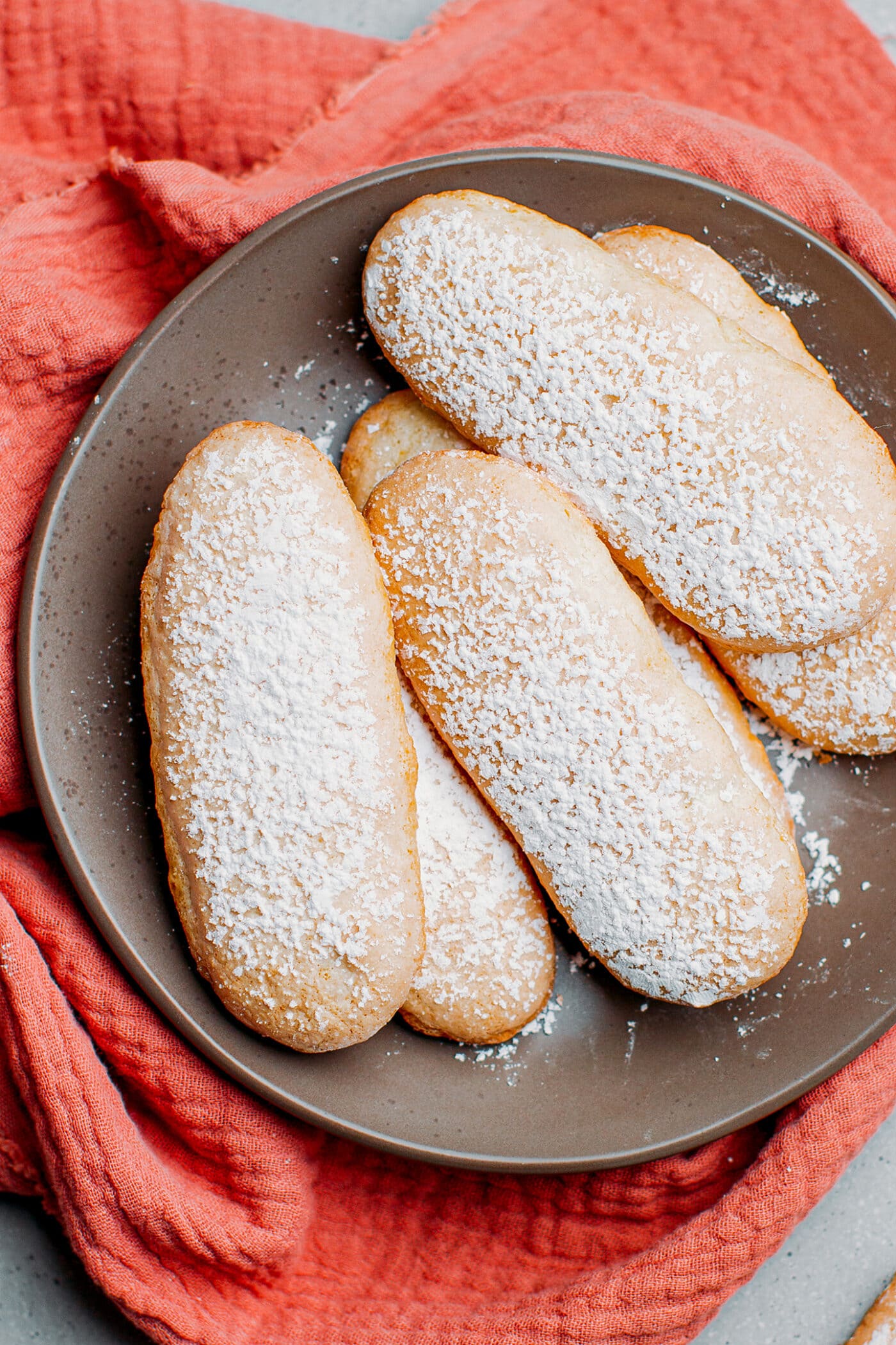 Vegan ladyfingers dusted with powdered sugar on a plate.