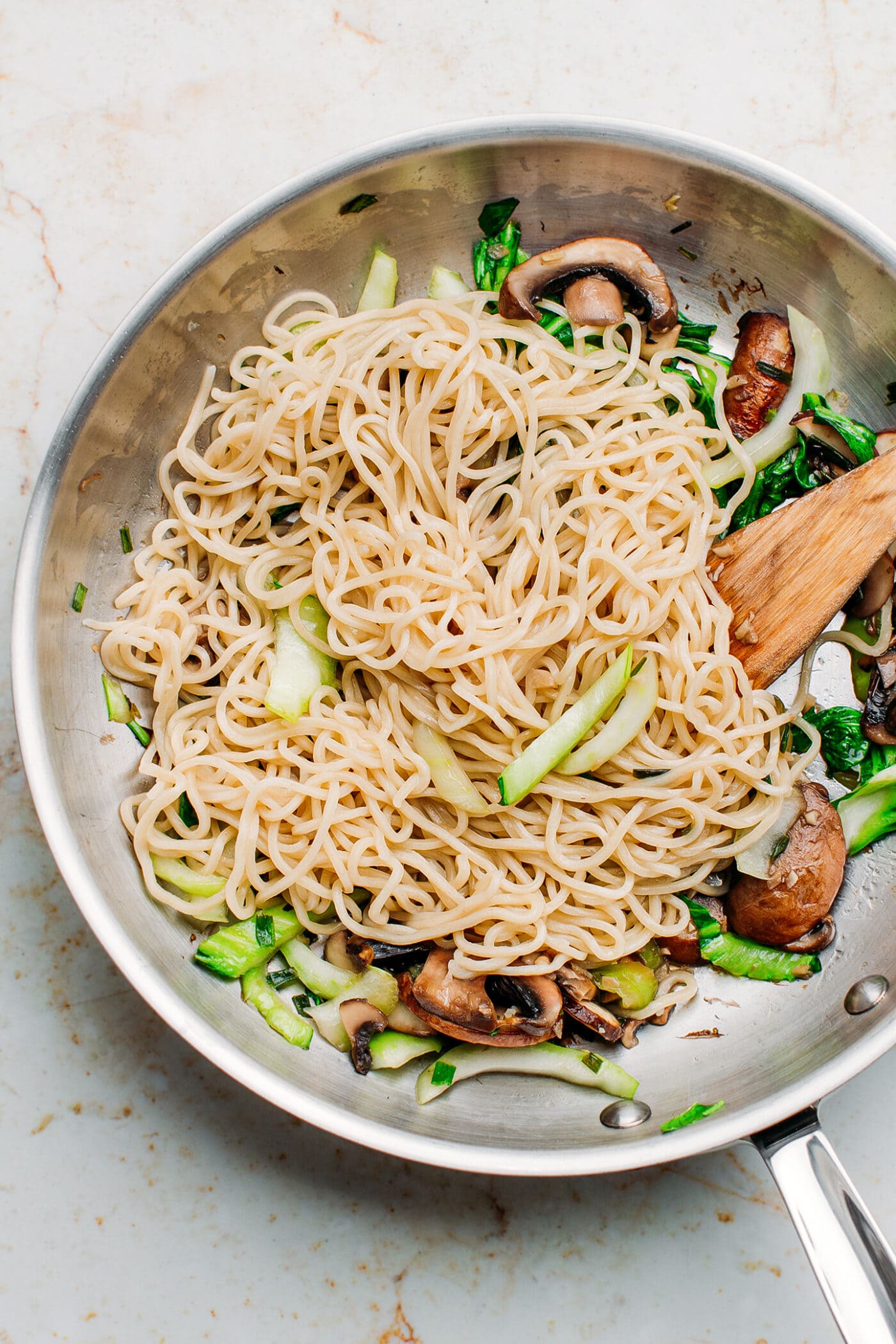 Noodles, mushrooms, and pak choi in a pan.