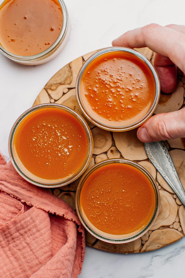 Three caramel pots de crème on a wooden board.