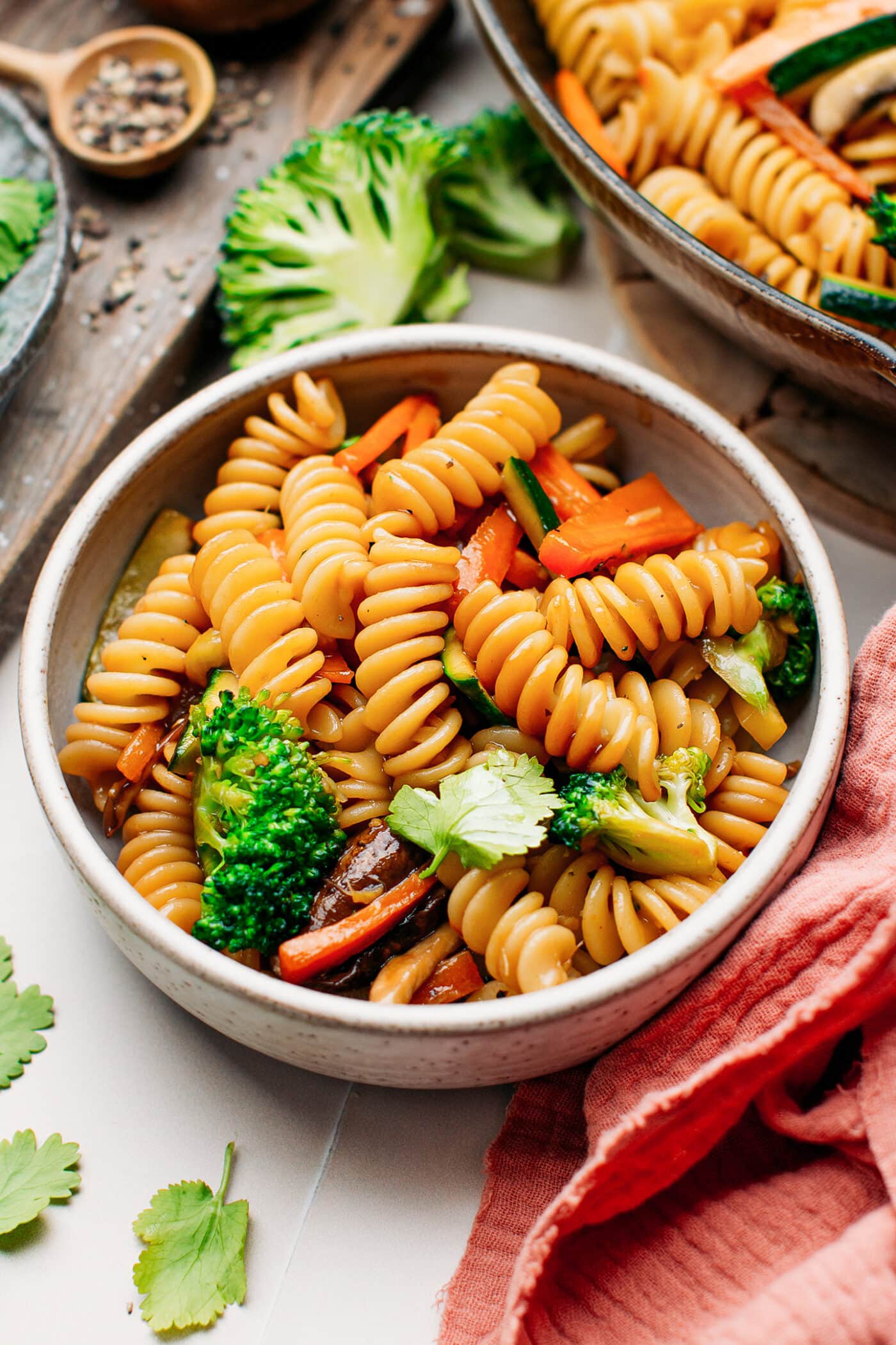 Fusilli pasta stir fry in a small bowl with broccoli and cilantro.