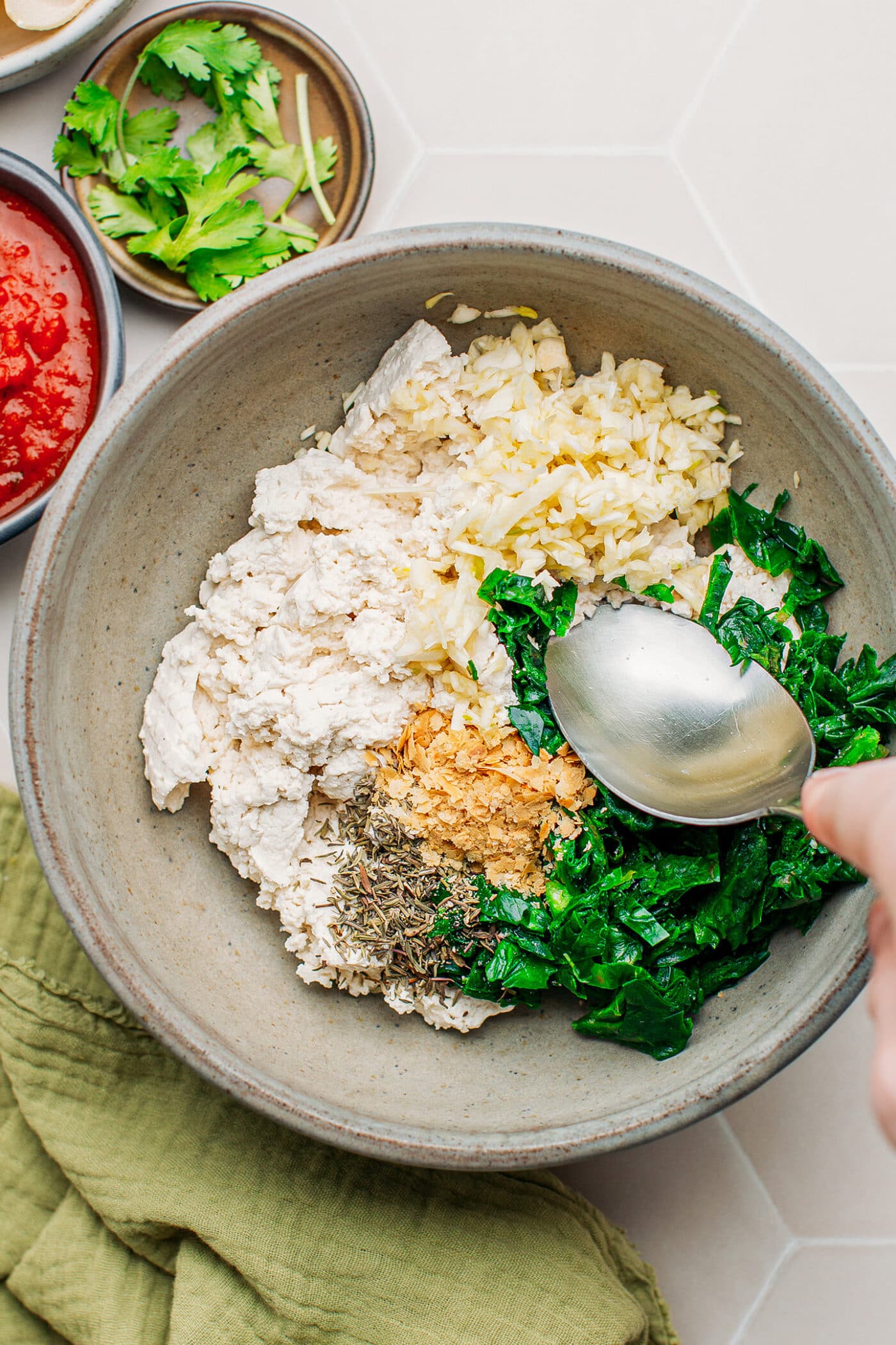 Combining ricotta, garlic, spinach, nutritional yeast, and herbs in a bowl.