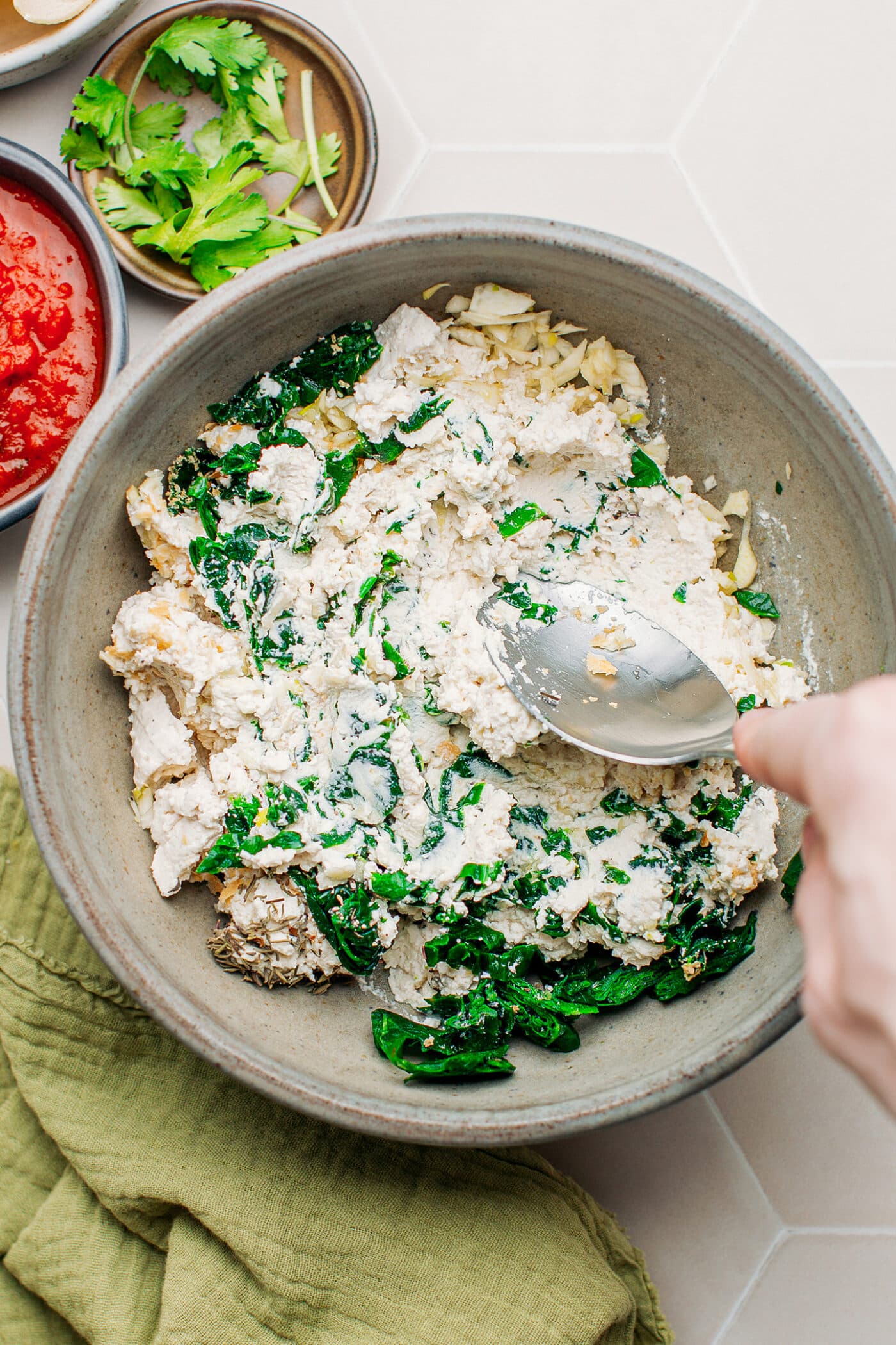 Stirring vegan ricotta with spinach and garlic in a bowl.