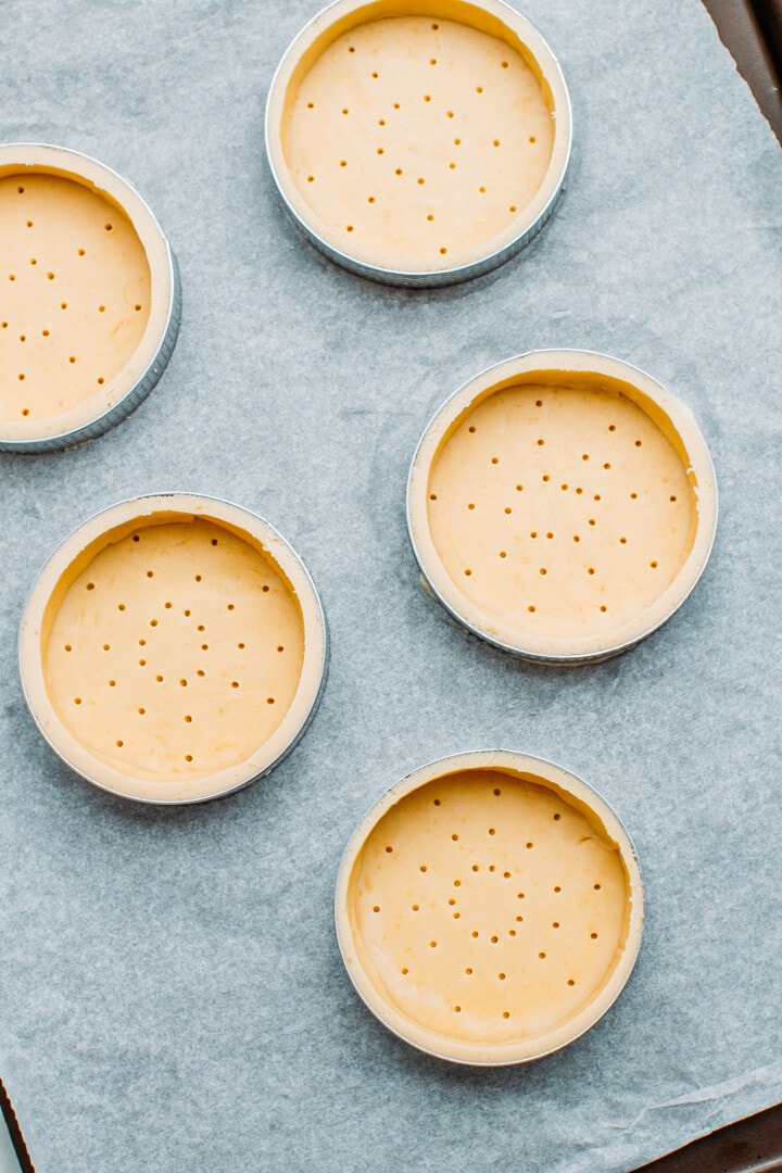 Unbaked tartlet shells on a baking sheet.