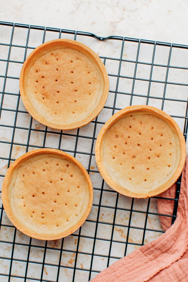 Three tartlet shells on a cooling rack.