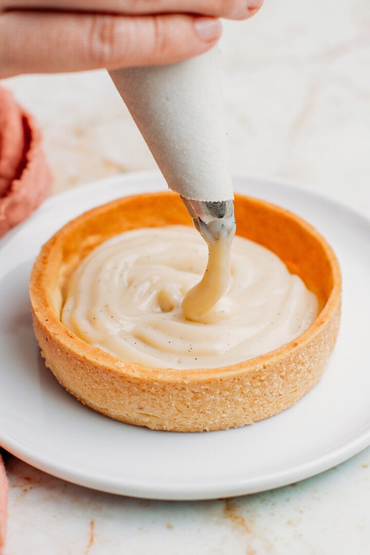 Piping vanilla pastry cream into a tartlet shell.