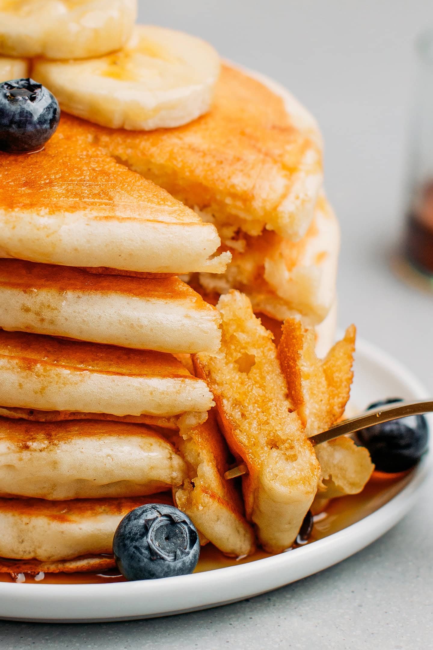Close-up of a a sliced stack of pancakes drizzled with maple syrup. 
