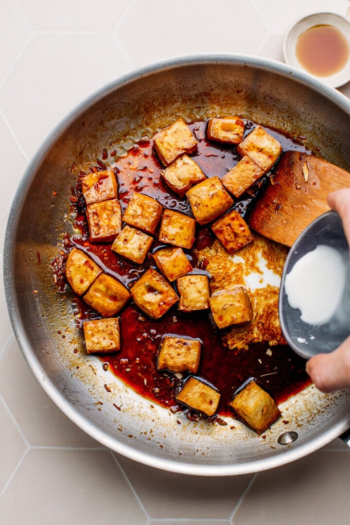 Pouring a cornstarch slurry into a pan containing tofu.