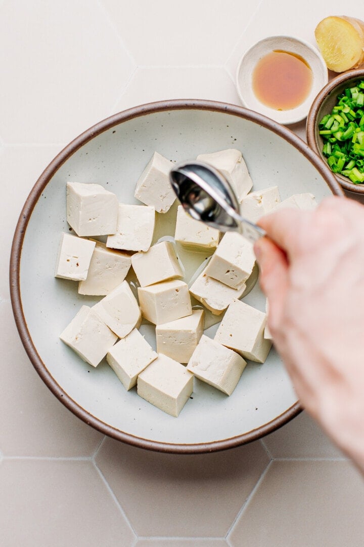 Pouring oil over tofu cubes.