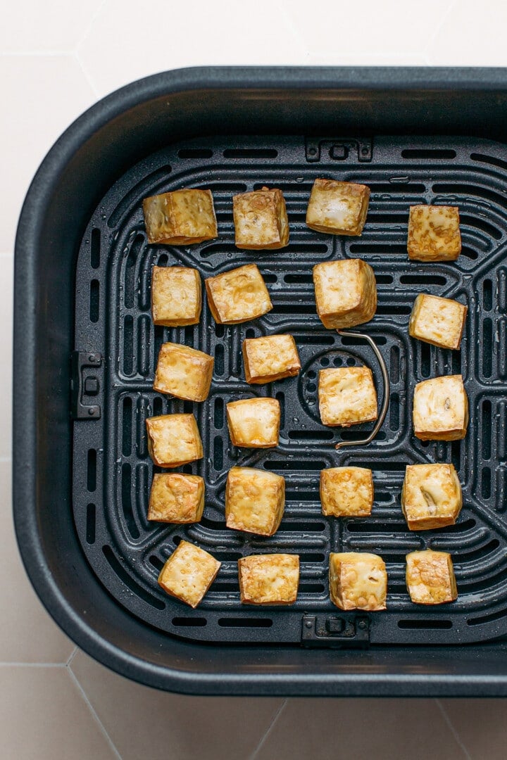Air-fried tofu in the basket of an air fryer.