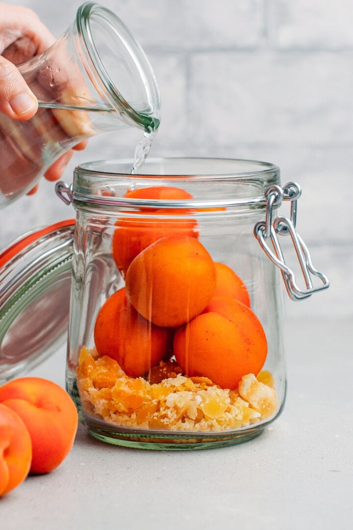 Pouring vodka over apricots, in a jar.