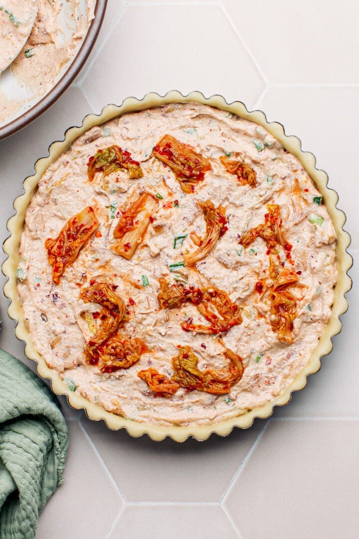 Unbaked kimchi quiche topped with kimchi pieces.