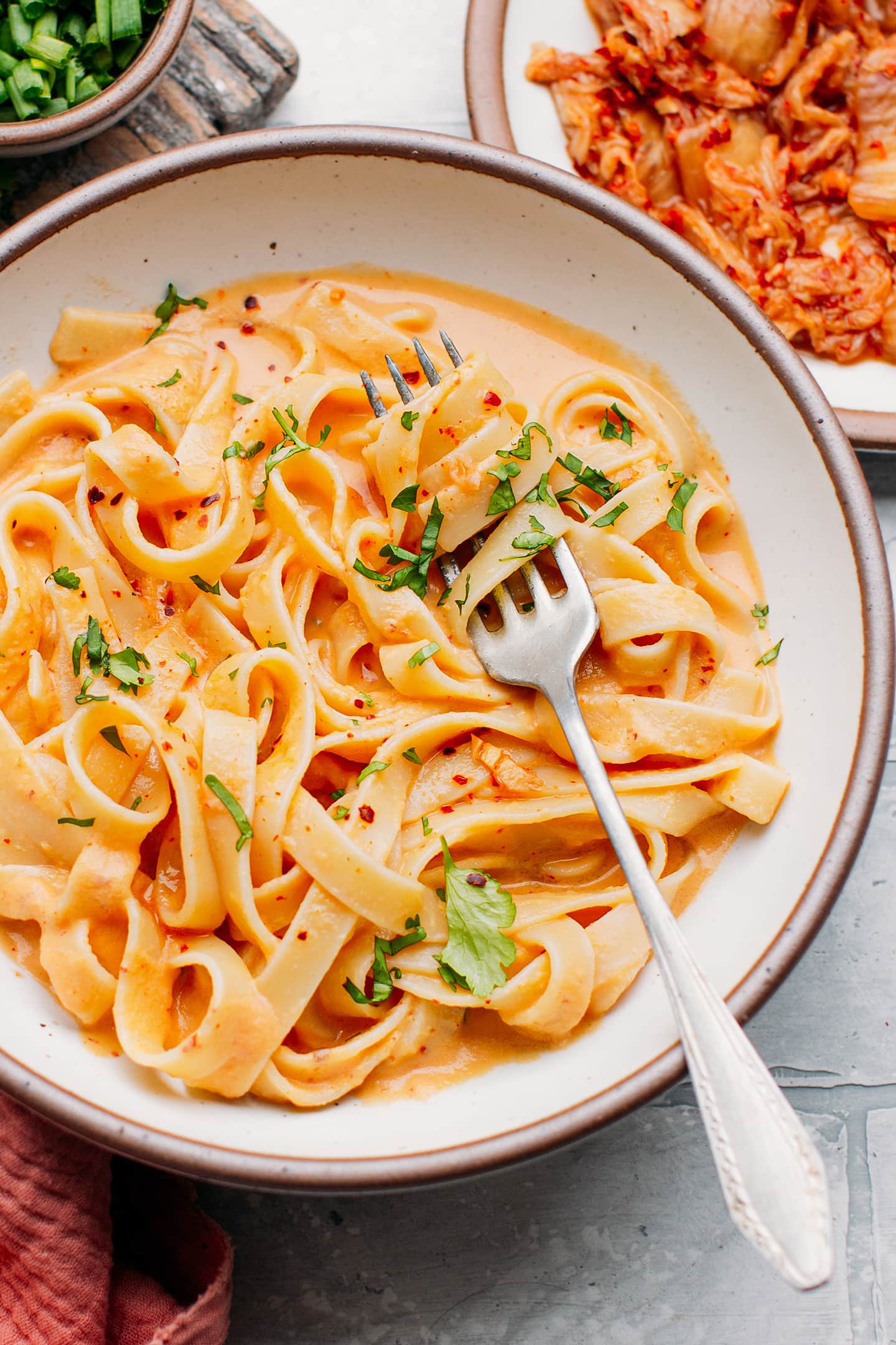 Fettuccine coated with kimchi sauce and topped with chopped cilantro.