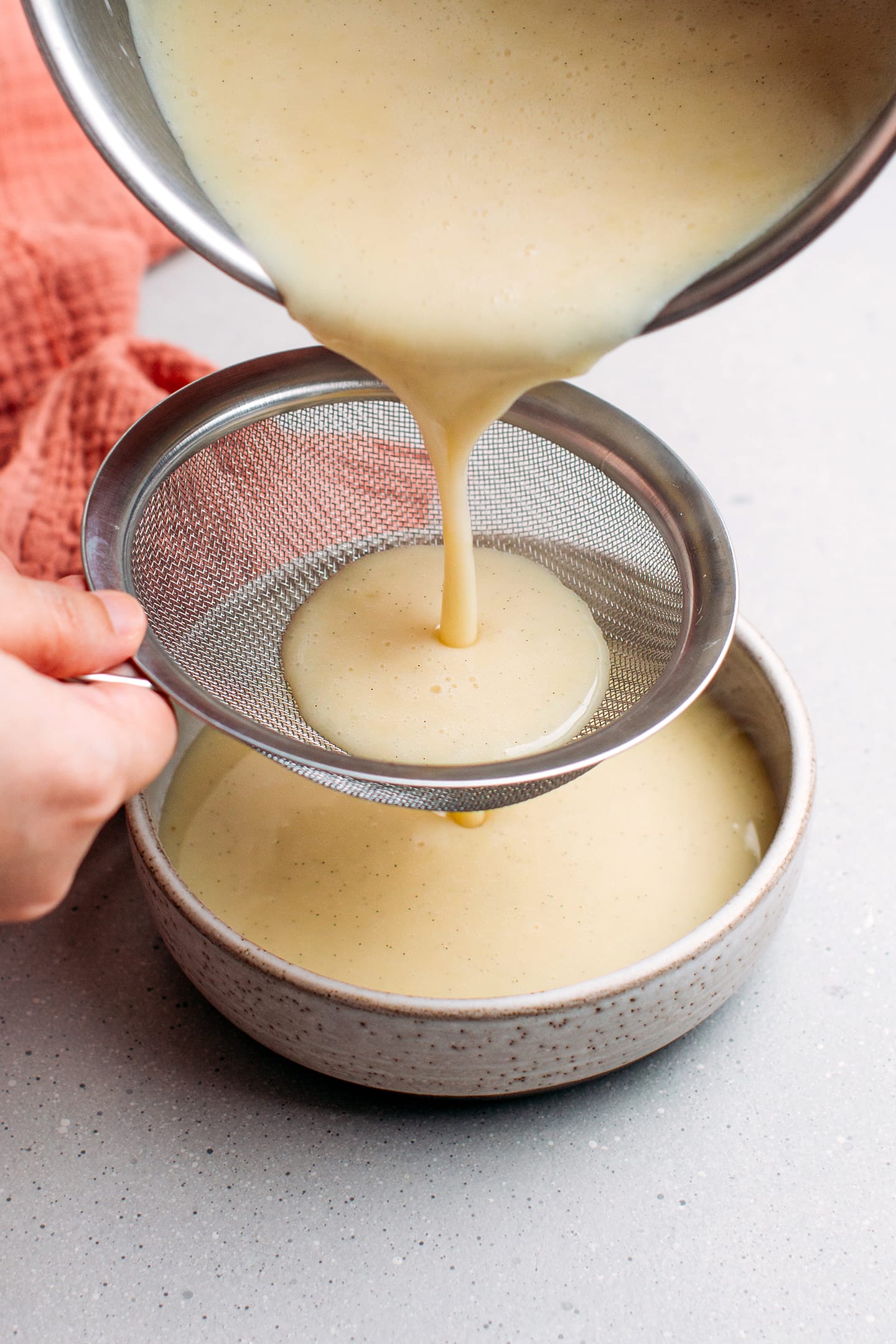 Straining vanilla custard through a fine-sieve mesh.