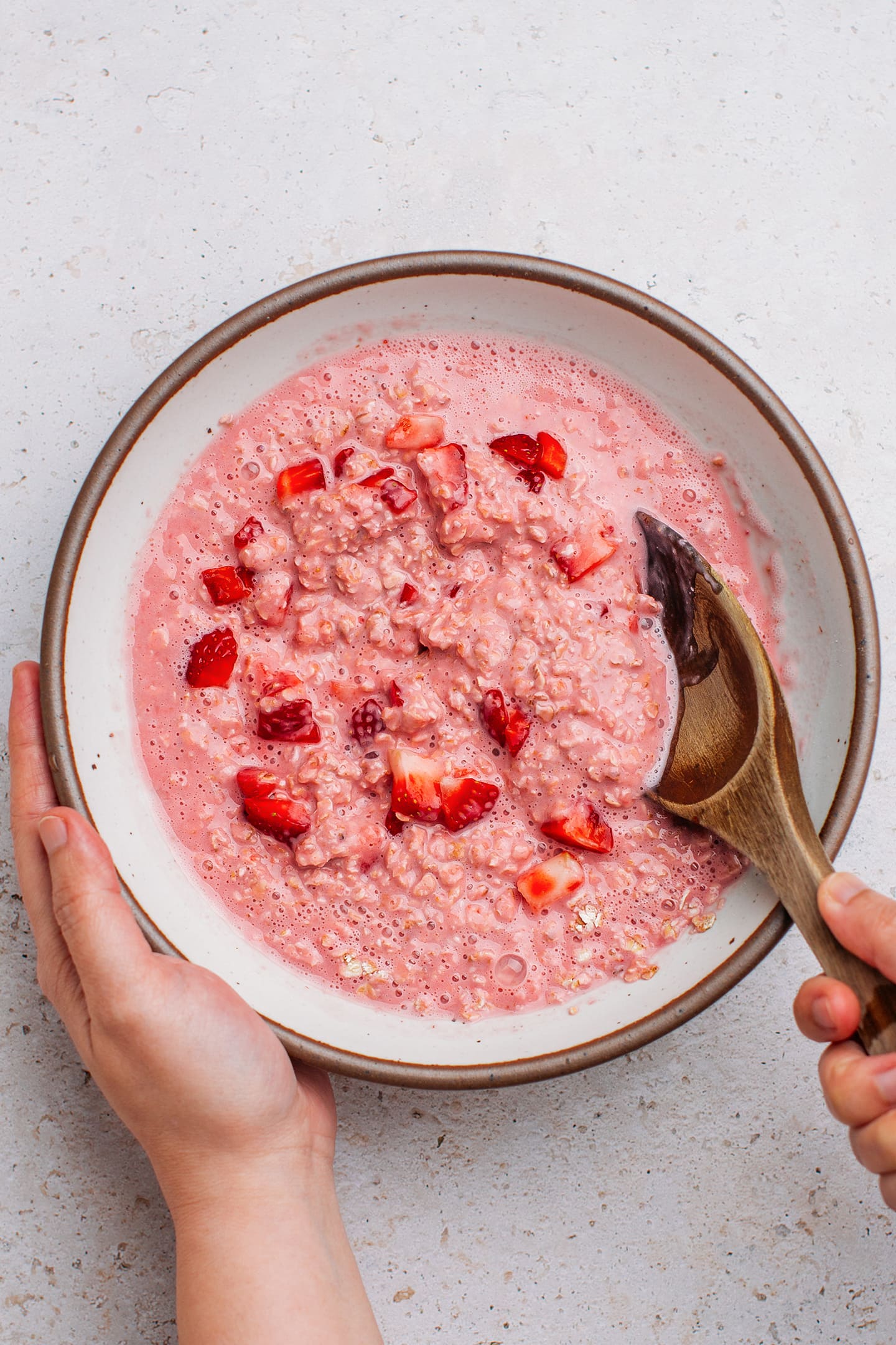 Stirring diced strawberries with oatmeal in a bowl.