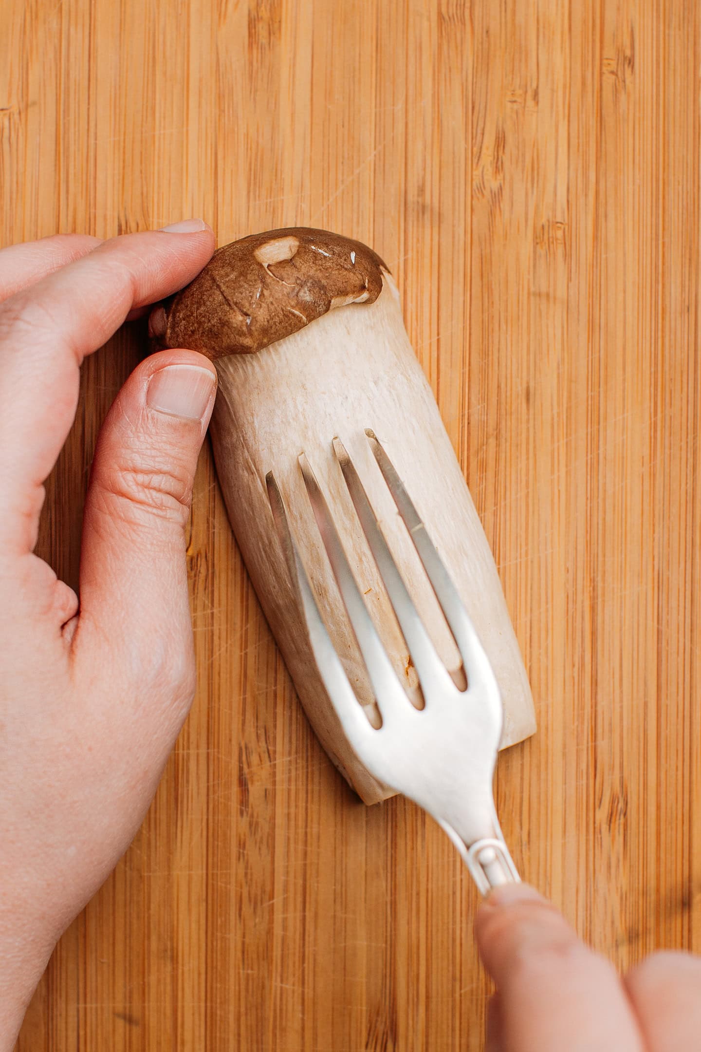 Using a fork to shred a king oyster mushroom.