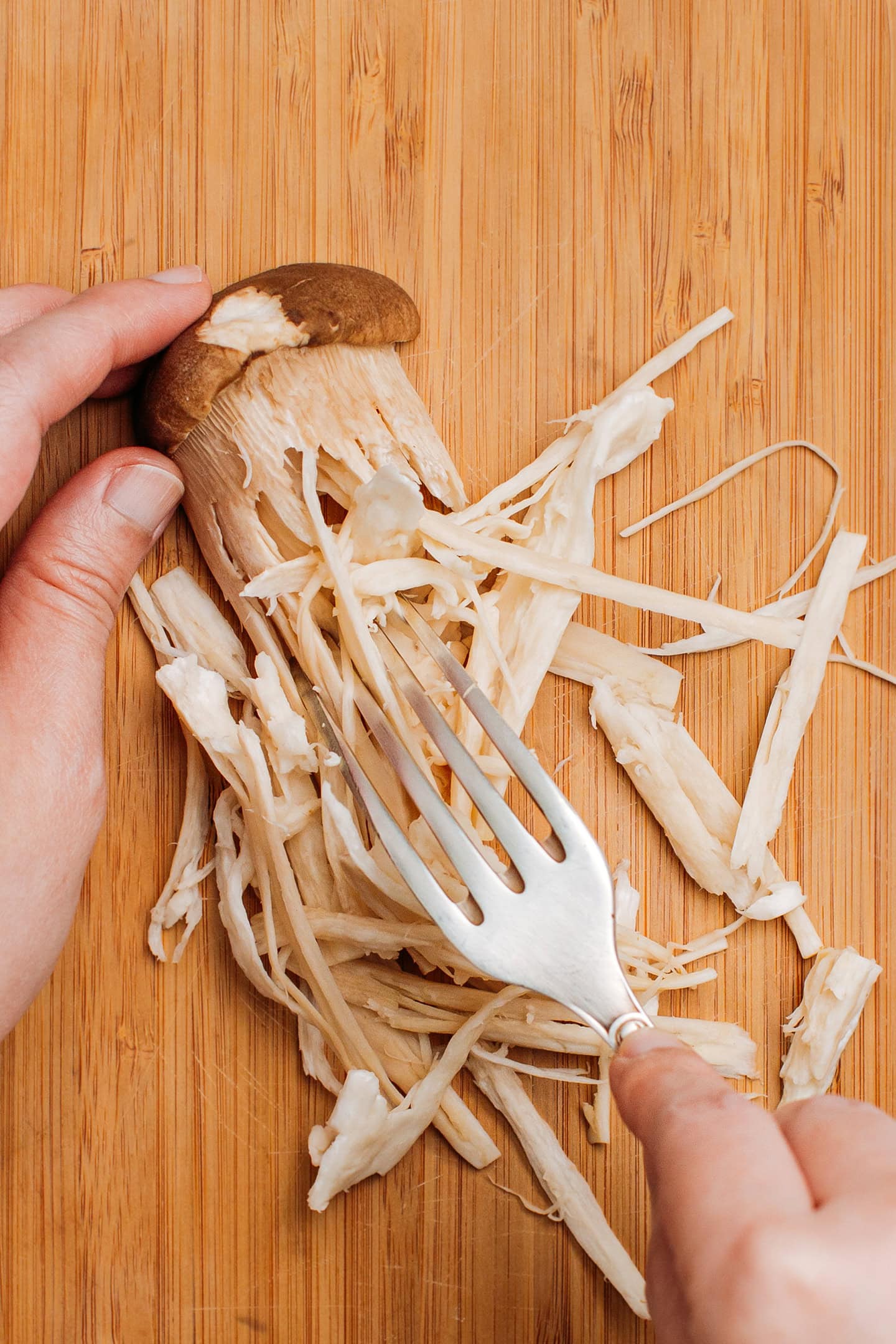Shredding a king oyster mushrooms using a fork.