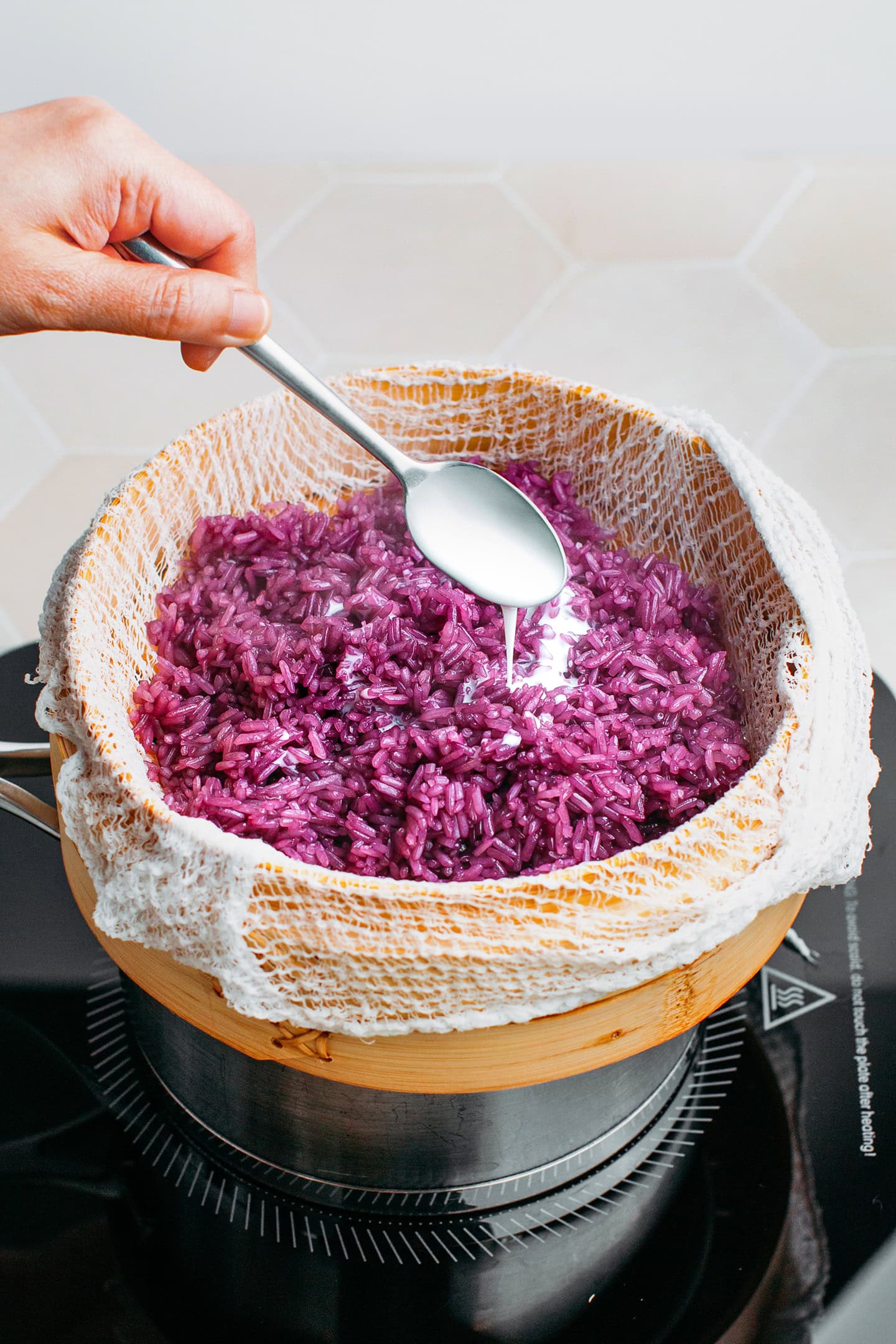 Pouring coconut milk over sticky rice in a steamer.